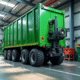 Camion ampliroll soulevant un conteneur vert dans une usine de recyclage